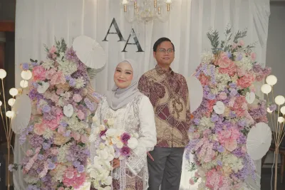 Andrika dan Aliva berdiri berdampingan di depan latar bunga bermonogram AA.